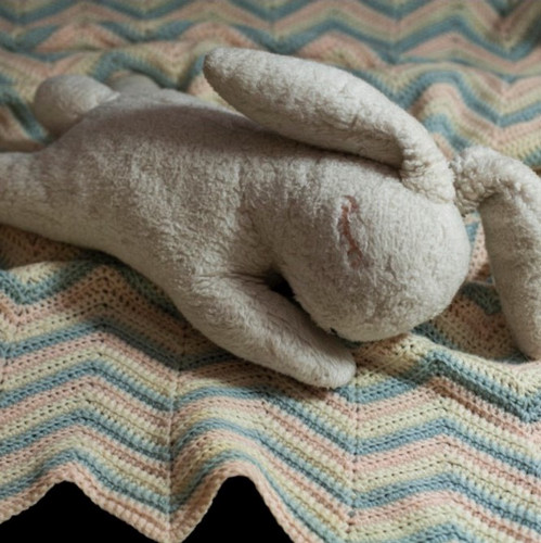 stuffed bunny laying down with a patterned blanket 