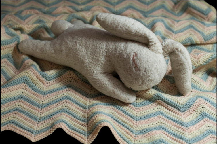 stuffed bunny laying down with a patterned blanket 