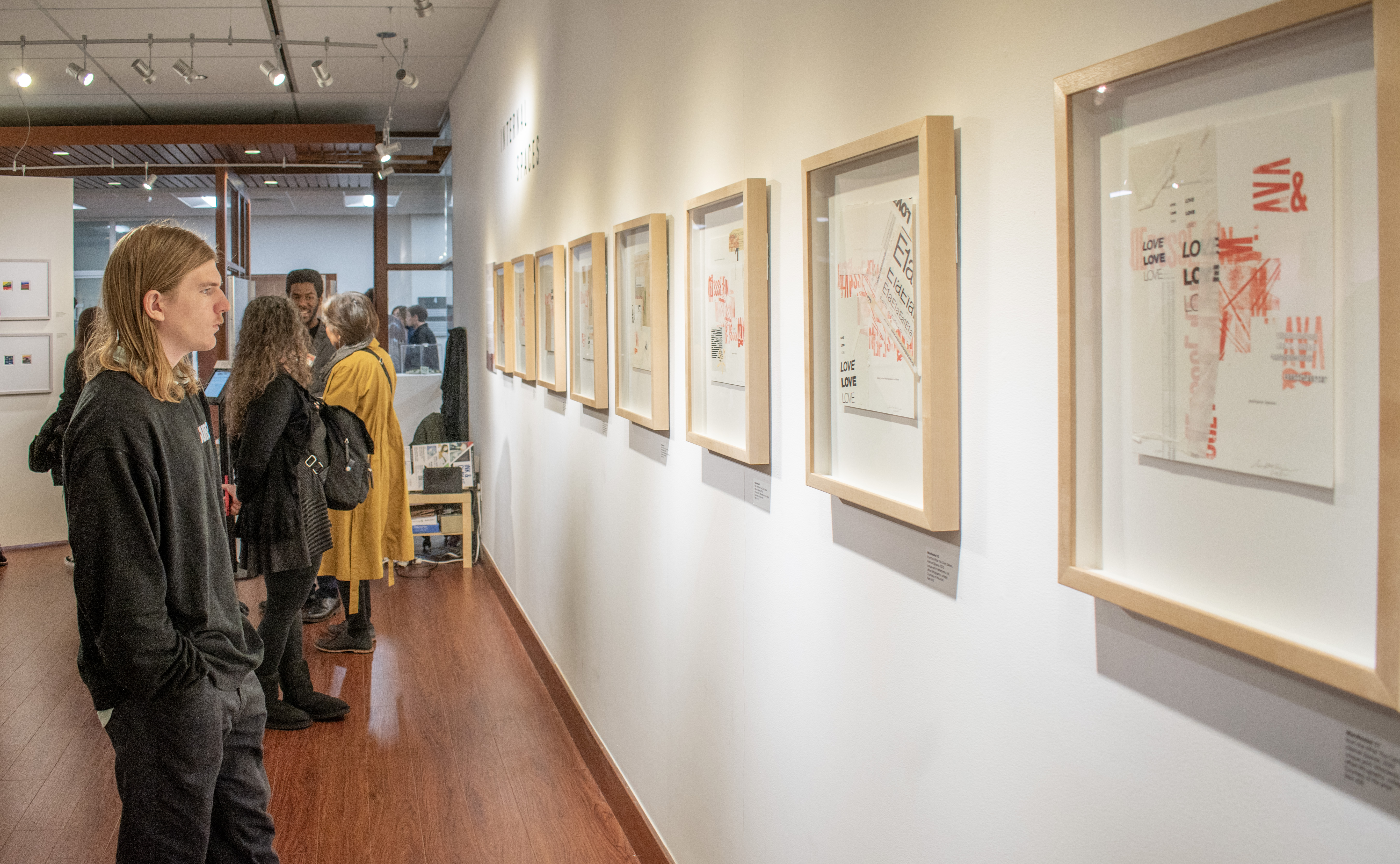 A photograph of a gallery guest staring at the exhibited pieces on the wall