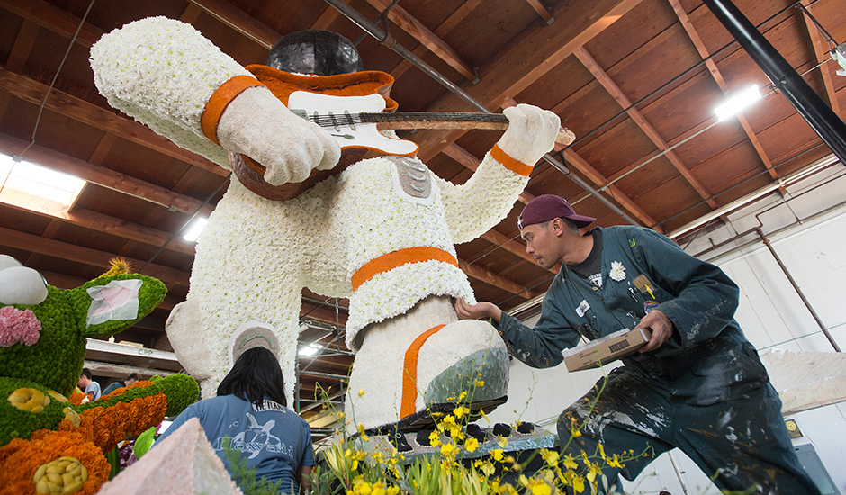 A male student decorates a Cal Poly Universities Rose Float. 