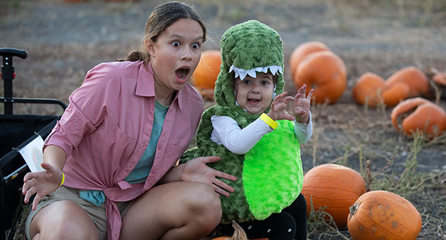 A mother and her child in a Dinosaur costume at the pumpkin patch.