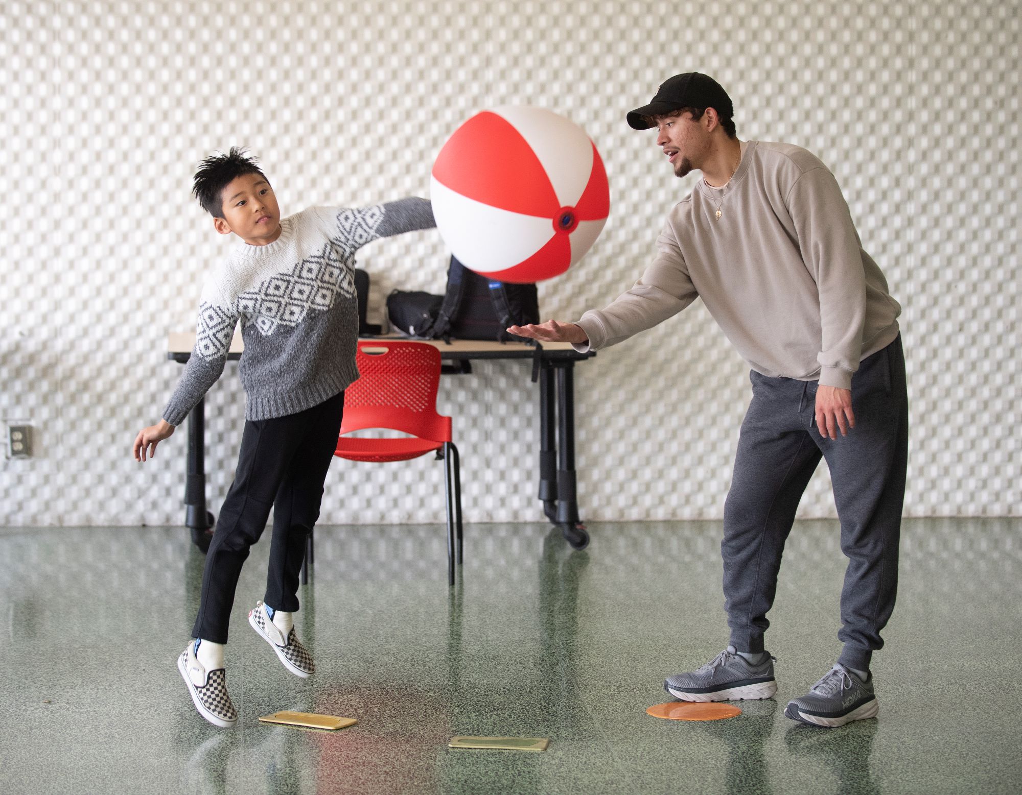 Male student helps a male child using a ball during a session at the Motor Development Clinic.