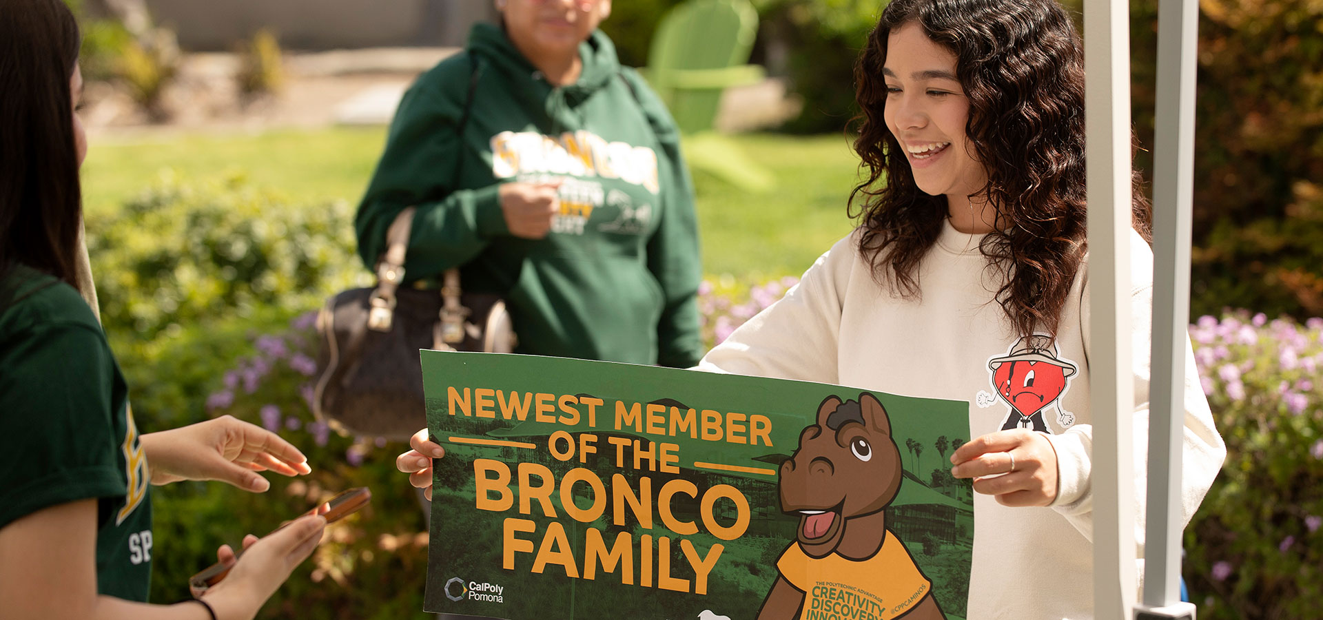 A girl holds a sign that says Newest Member of the Bronco Family.