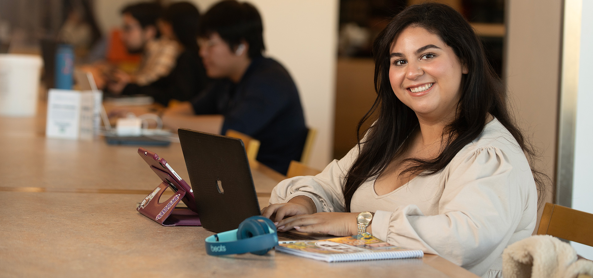 Female student sits at a table with her laptop and smiles.