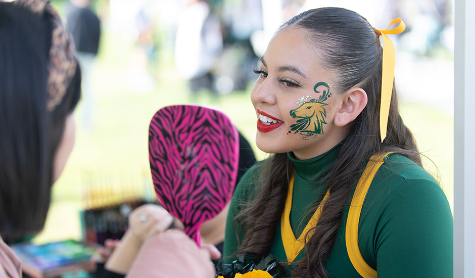 A female cheeleader gets her face painted with glitter during the Green and Gold party.