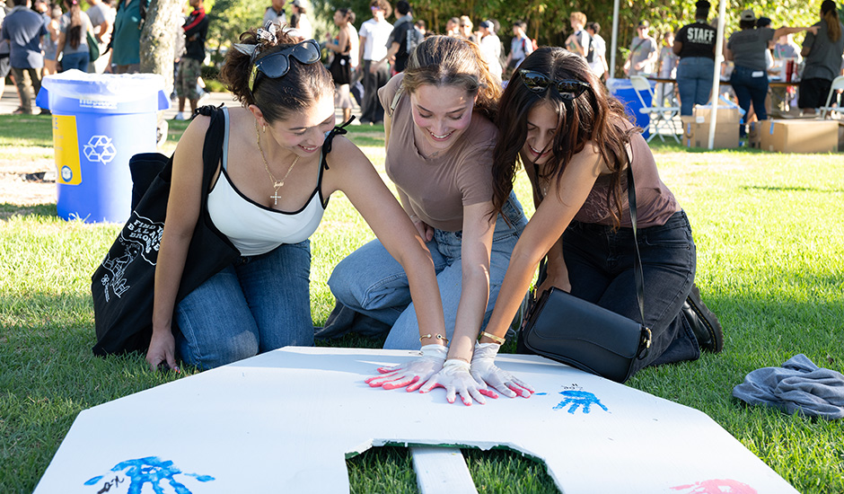 A group of female students put hand prints on welcome letters during New Student Convocation activities.