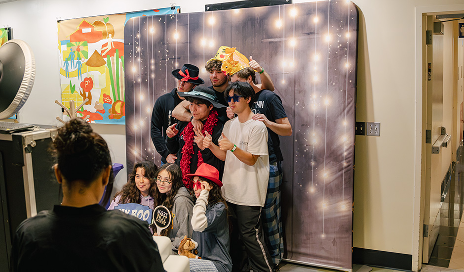 A group of male and female students pose at a photo booth station with photo props