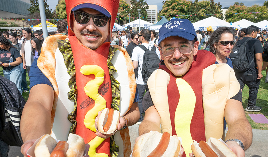 Two male students dressed as Hot Dogs hold two hot dogs during the 2025 Hot Dog Caper.