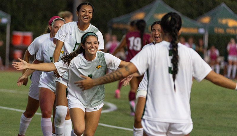 Members of the Women's Soccer team celebrate after scoring during a game.
