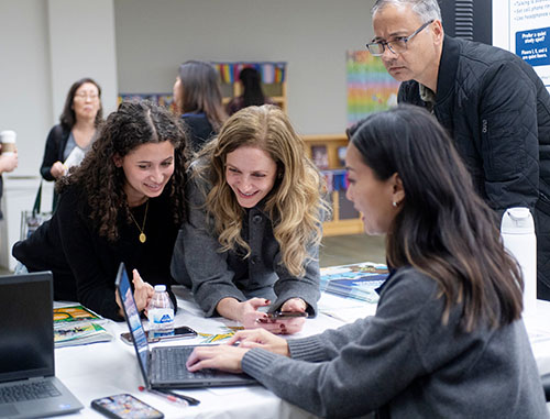 four people gather around a laptop