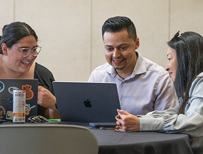 three people around a table working on laptops