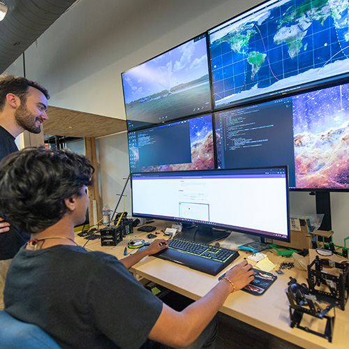 student standing, another seated, both looking at five large computer displays