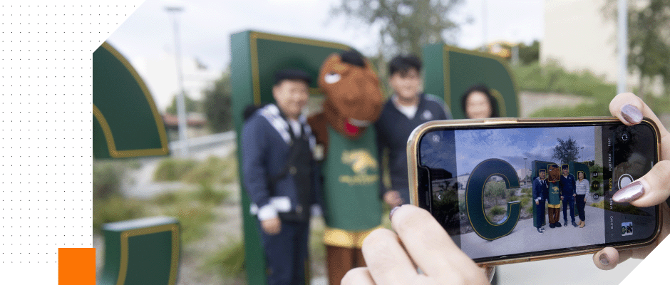 People stand in front of the CPP letters with Billy Bronco the university mascot for a photo using a smartphone