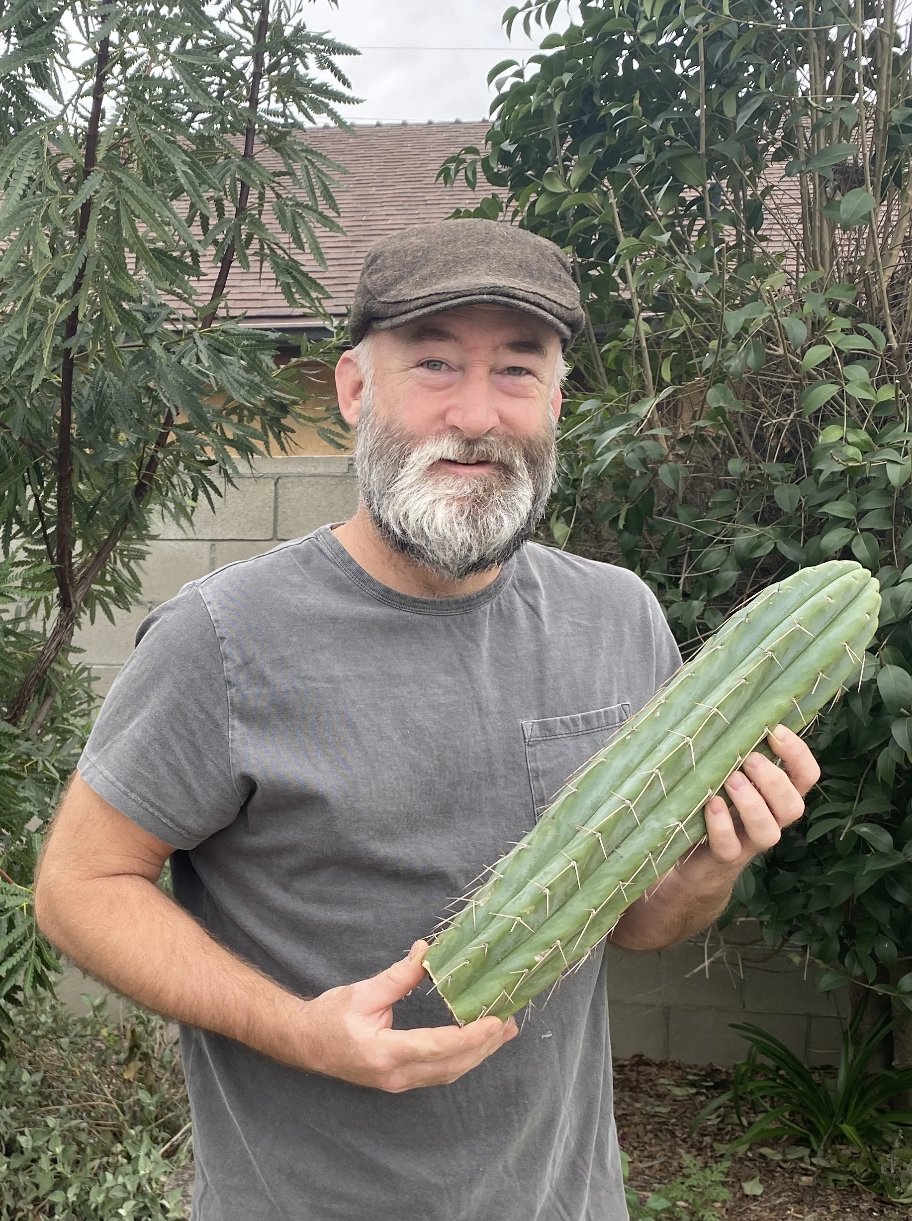 An older gentleman with a white beard holding up a cactus.