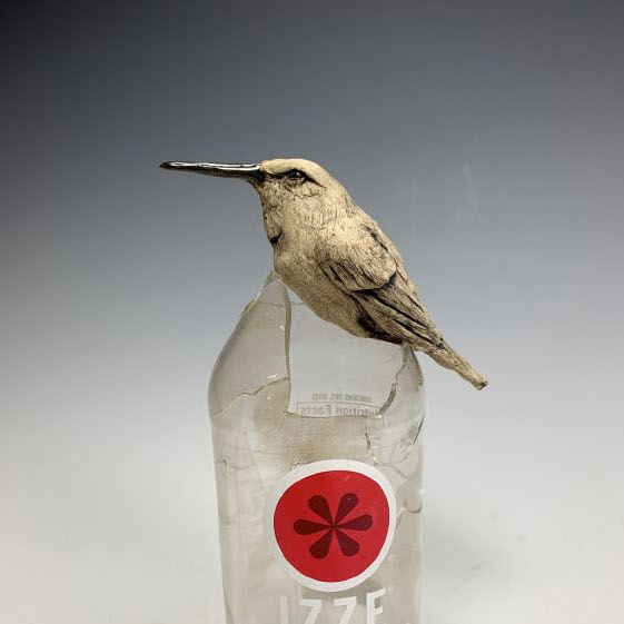 Deana Bada-Maloney, Nectar, 2019. Stoneware and found objects. 7.5 x 4 x 2.5" Courtesy of the artist. A bird sitting on top of a cracked glass bottle of sparkling pomagranite.