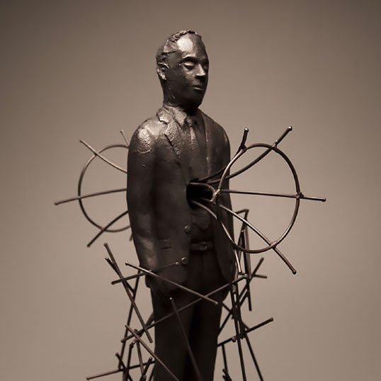 Brian Christensen, Maintaining a Tenuous Construct, 2017. Ceramic, steel. 25 x 10 x 13” Courtesy of the artist. A sculpture of a man with sticks surrounding him and a wires going through his body.