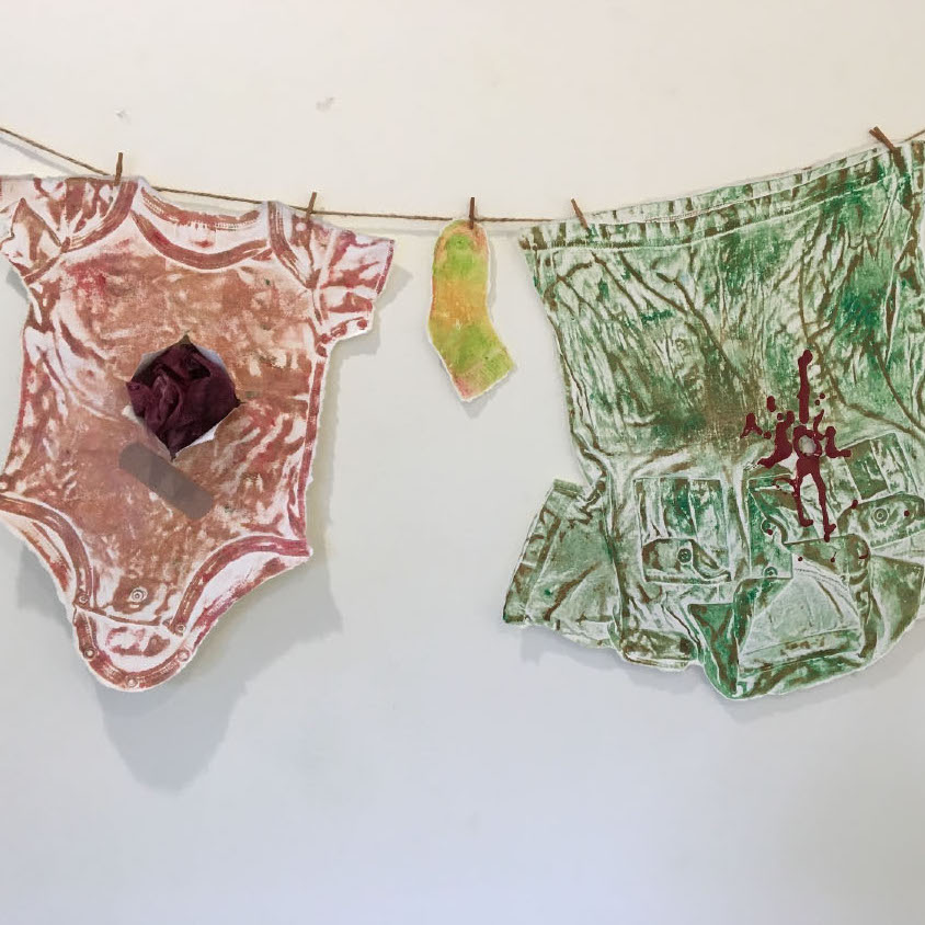 Carolyn Liesy, School Shootings: Hung Out to Dry, 2018. Collograph, clothes pins, rope. 24 x 67 x 3“ Courtesy of the artist. Two shirts hanging on a wire.