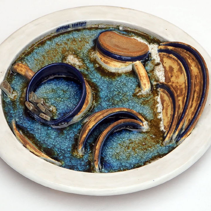 Connie Major, T.V. Time, 2018. Stoneware clay, high-fire glazes, glass. 15 x 15 x 3” Courtesy of the artist. A sculpture of plates, cups, and eating utencils
