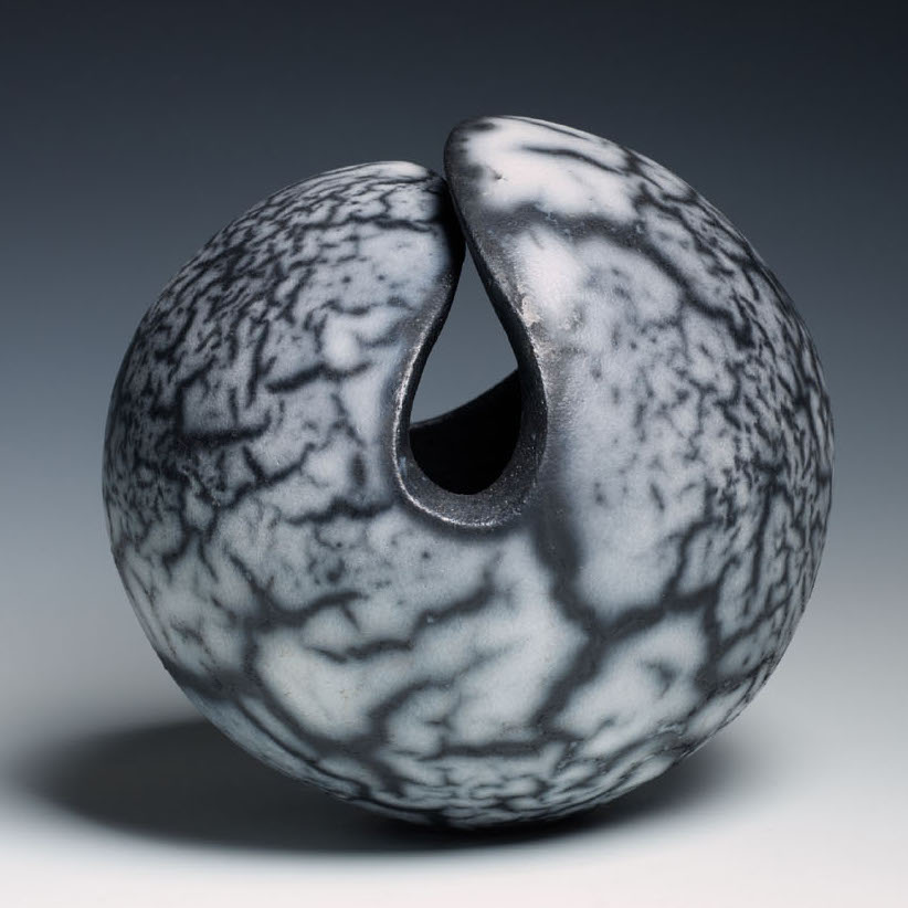 Katie Yang, Chance, 2018. Clay infused with smoke. 5.75 x 6 x 5.5” Courtesy of the artist. A ceramic sculpture of a round bead-like object with a curved opening that folds.