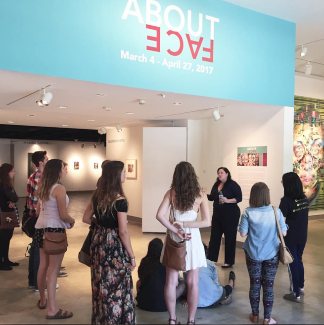 Photo of Guided Group Tour of About Face (2017) exhibition with visiting students from another local off-campus university with Gallery Curator, Michele Cairella Fillmore. Exhibition featured the work of Justin Bower, Rebecca Campbell, Salomon Huerta and Roni Stretch.