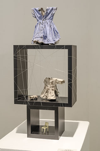Two dark colored square frames stacked onto one another. The one on top is larger than the one on the bottom. The top box has strings going in multiple directions around it. There are abstracts objects in both the openings.