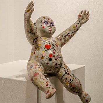 Frank Barron, Untitled. Is a figure sculpture that is sitting on a white stand. The figure has his arms ups and out.