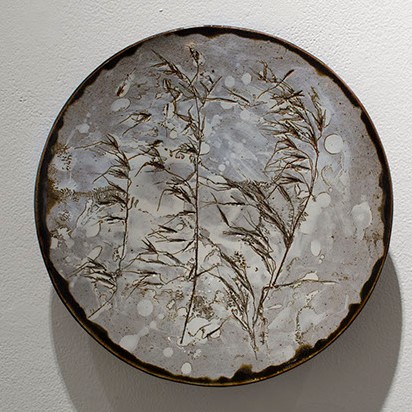 Doris Fischer-Colbrie, Winter Storm. A plate-like sculpture that has dark brown edges. The circle object has small branches in brown on it.