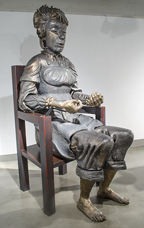 Carol Ann Klimek, "Meditator" sitting in a large chair, there is a statue of a figure meditating.