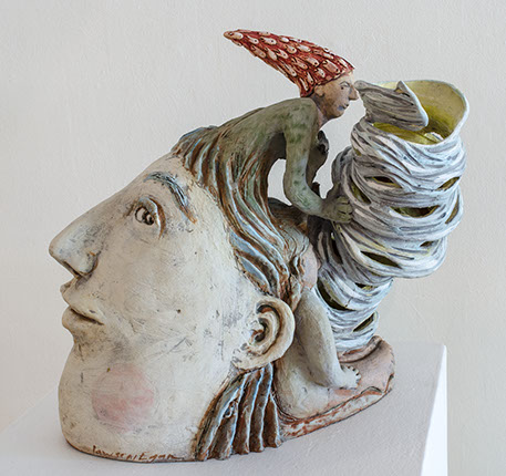 A sculpture of a very pale head, in the hair of the sculpture there is another creature growing out of it.