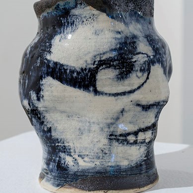 Monika Ozog, "Konrad" a black, white, and blue vase. On the vase there is a face of a young boy that is smiling and wearing glasses.