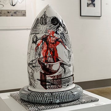Vince Palacios, "Alchemy Series: Preventive Measure, Pre-emptive Strike" This shows a rounded sculpture that comes to a point at the top. There are drawings of people and organic lines in red and black, with a white background.