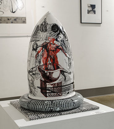 An abstract sculpture that is round, but comes to a point at the top. It is painted with red, white, and black illustrations with lines and figures.