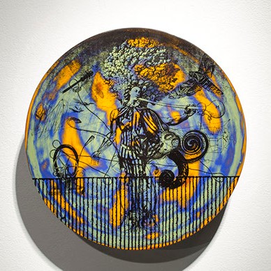 Vince Palacios, "Heraldry Series: The Final Trumpet" a plate-like- sculpture. It has vivid blues, orange, and green on it. In black there is an illustration of a figure in the middle.