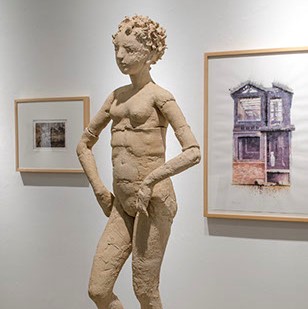 Judith Stewart, "Girl with Spiral Hair" is a human-sized tan sculpture. The figure is standing with one leg bent, and the other straight. Her hands are at her hips.