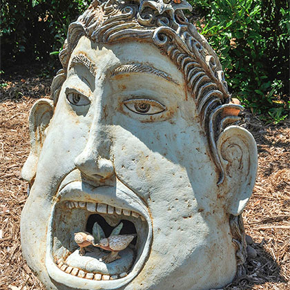 clay sculpture of (front) a head with an opened mouth with tiny birds inside and (back) standing human figures 