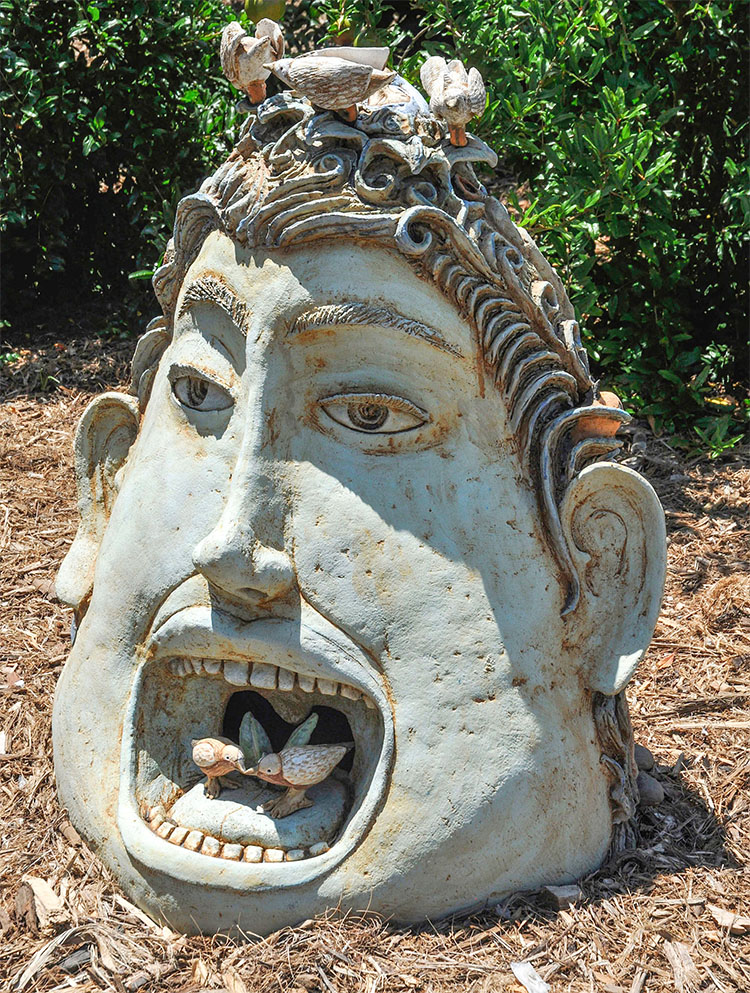 clay sculpture of (front) a head with an opened mouth with tiny birds inside and (back) standing human figures 