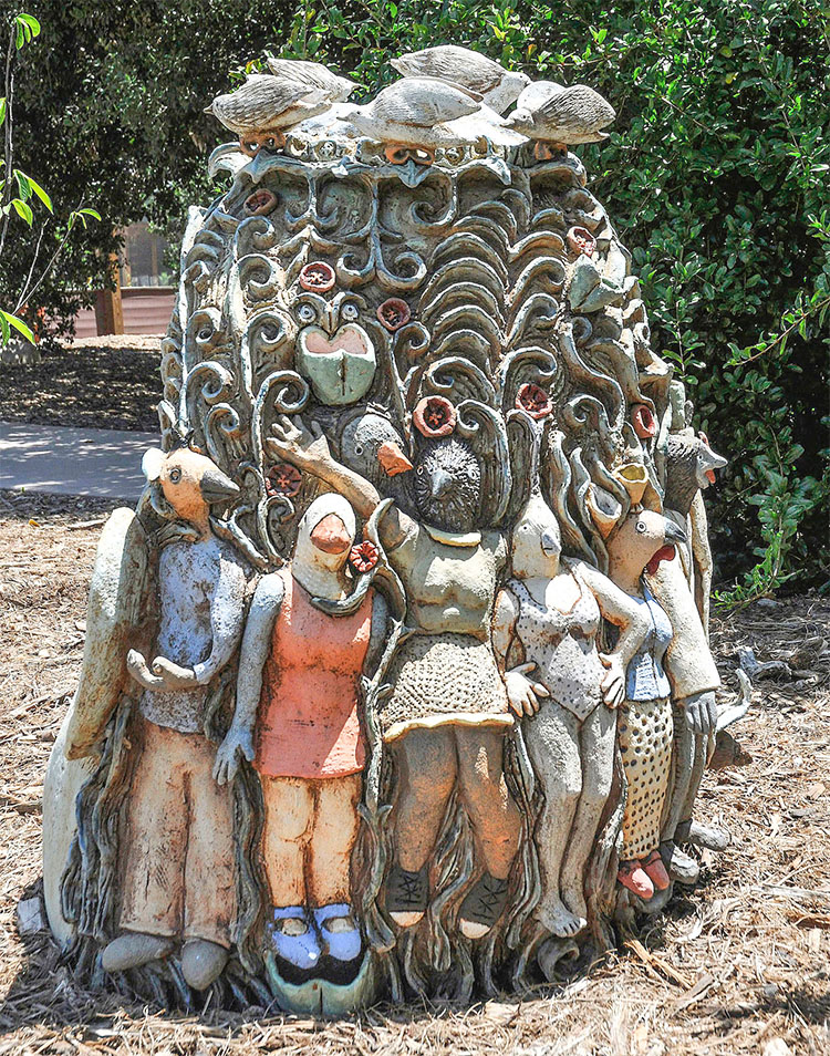 clay sculpture of (front) a head with an opened mouth with tiny birds inside and (back) standing human figures 