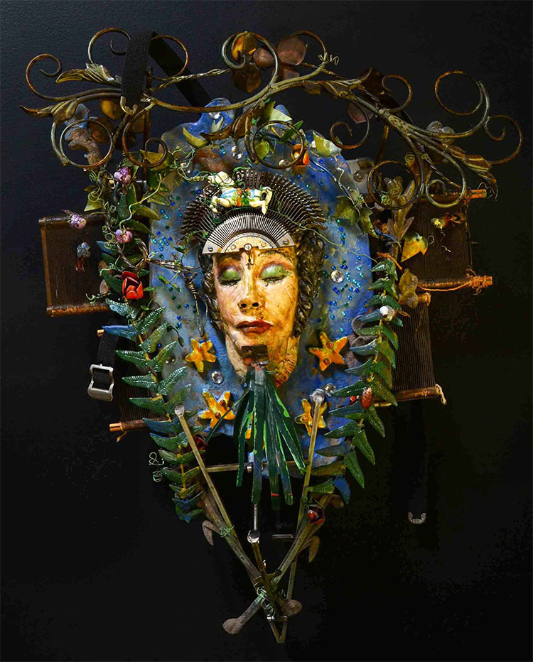assemblage: clay with encaustic, Hol-lywood film can, typewriter keyboard and found objects sculpture of a person surrounded by green foliage (looks like a displayed wreath)