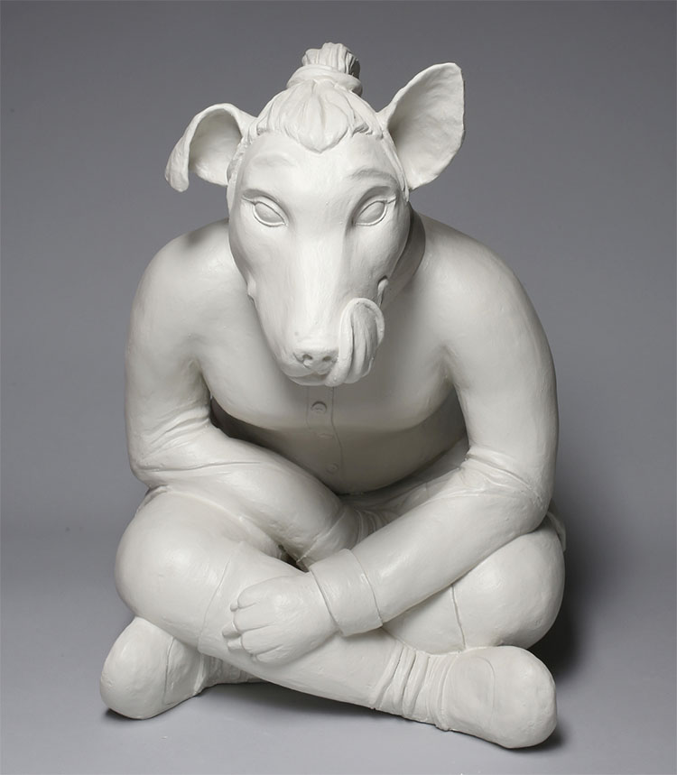 white ceramic sculpture of a dog  with a man bun sitting crisscross like a human and a tongue sticking up, licking its lips as though it is looking at something yummy to eat