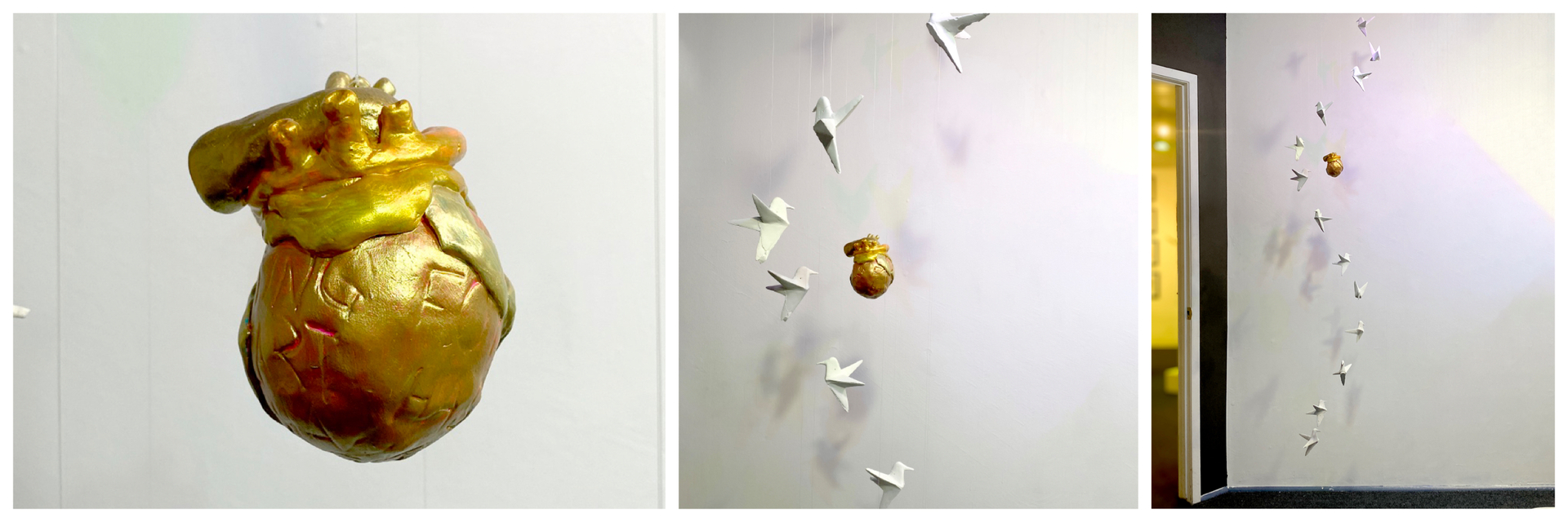 a suspended golden human heat with white paper-like cranes suspended around the heart. 