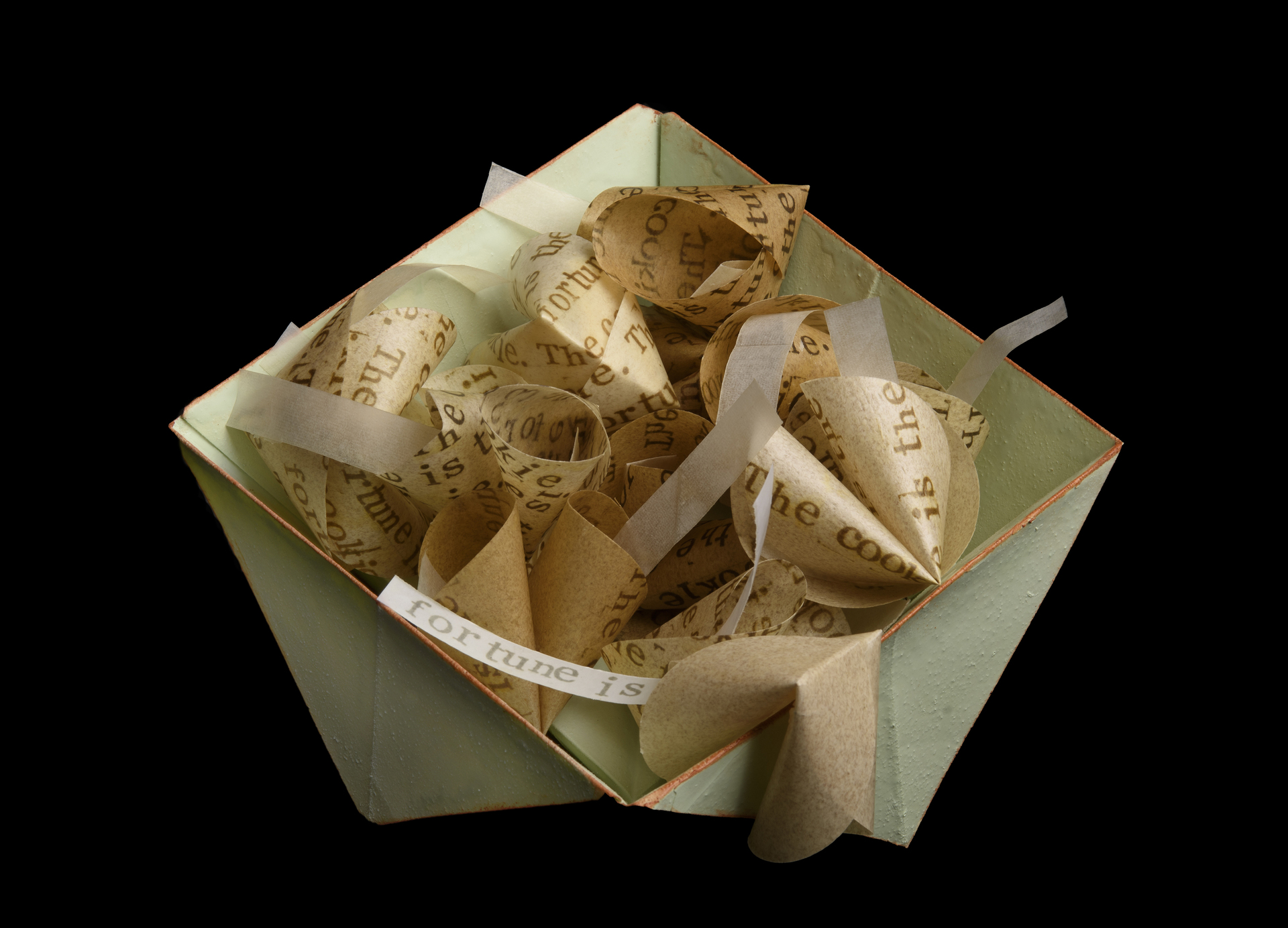 a mint green, paper oragami bowl holds multiple fortune cookies with handpritned messages on them that say, "The fortune is the cookie. The cookie is the fortune," on both the fortune cookie and the paper inside. 