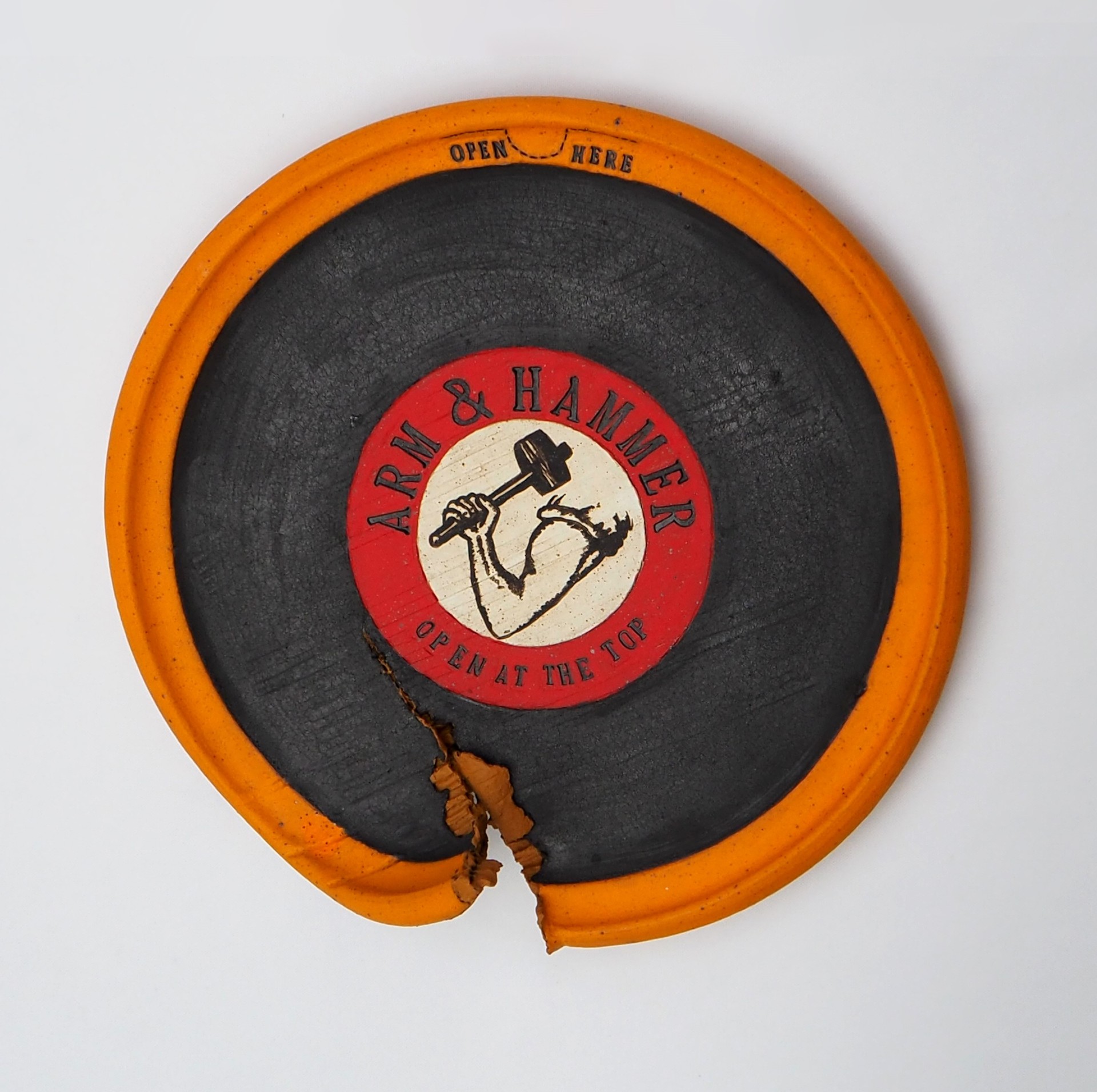  a circle plate with the "Arm & Hammer" logo on top with a rip towards the bottom of the plate.