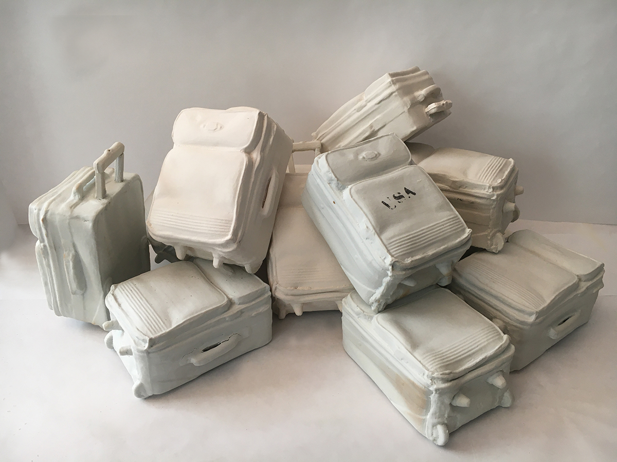  a sculpture of a pile up of suitcases. They are all white. One suitcase has 'USA' stamped on it in black.