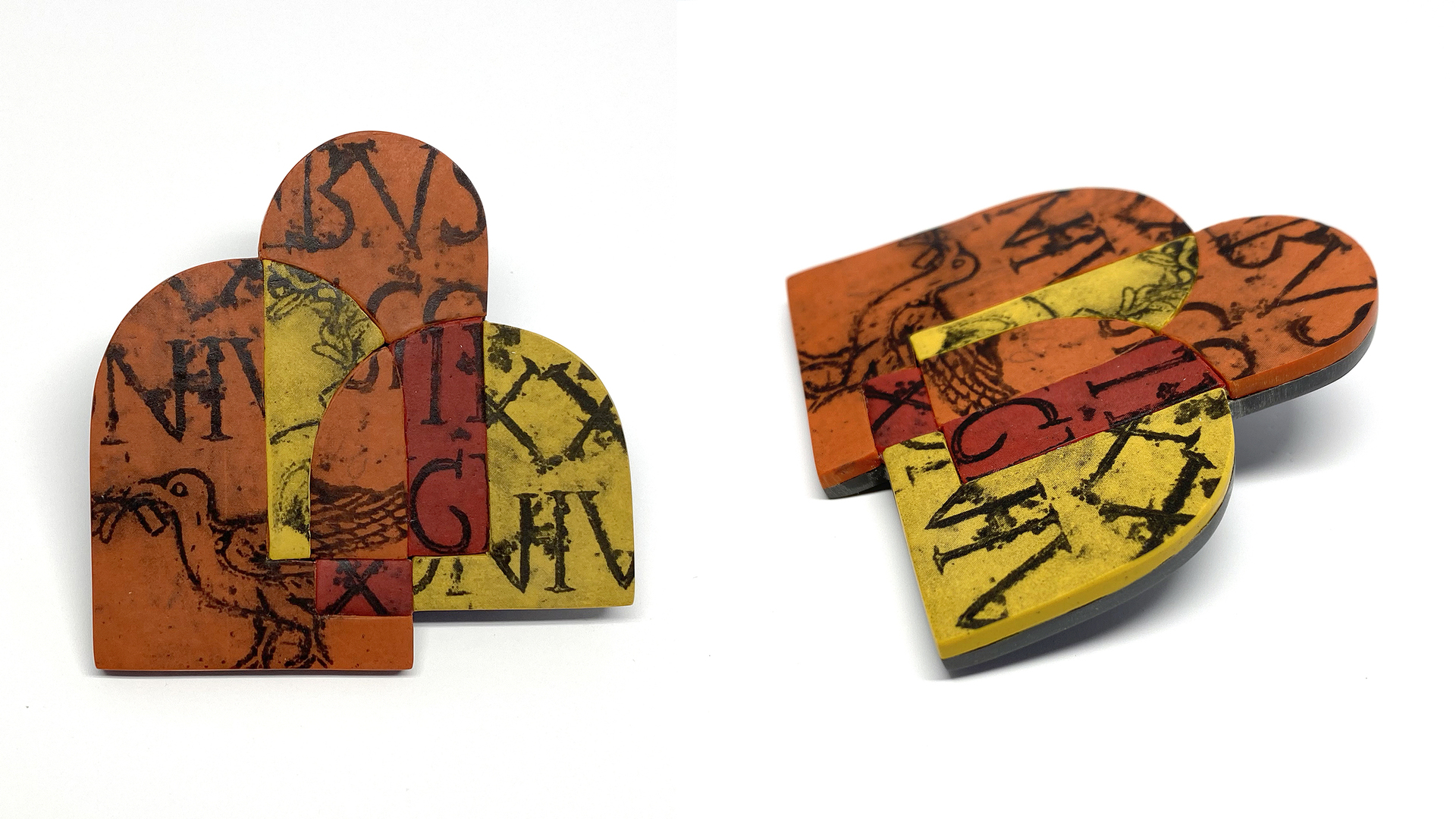 Clay object of 3 overlapping arches of different heights and widths. Two are orange and one is yellow, but the overlpping areas are yellow, red, and orange. There are black letterforms and a drawing of a bird on the piece.