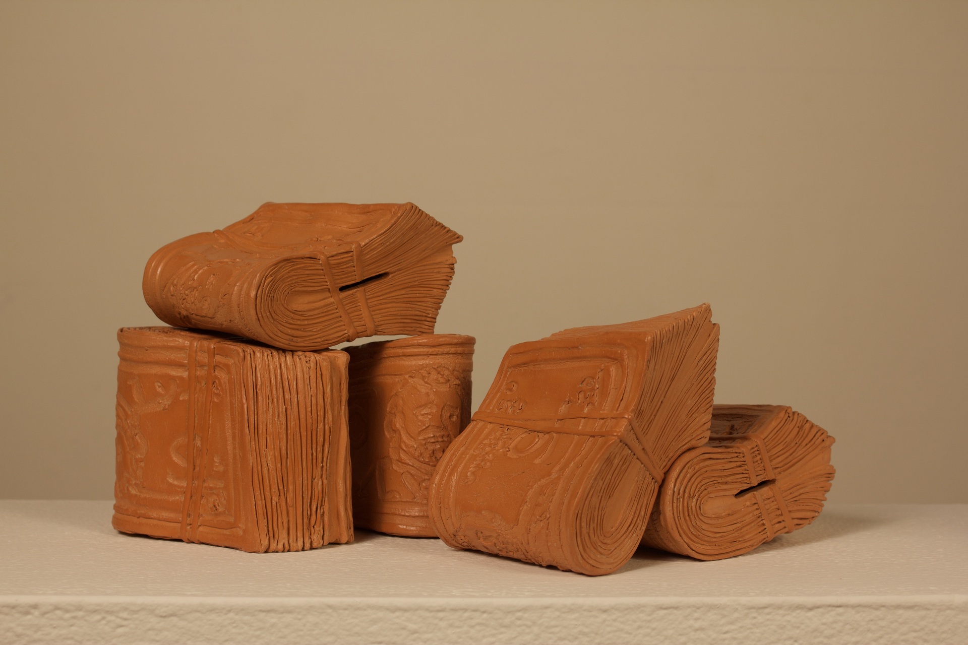 burnt orange colored clay sculptures that look like wads of cash rubber banded together. There are 5 different 'wads' of cash made of clay sitting around and resting on each other.