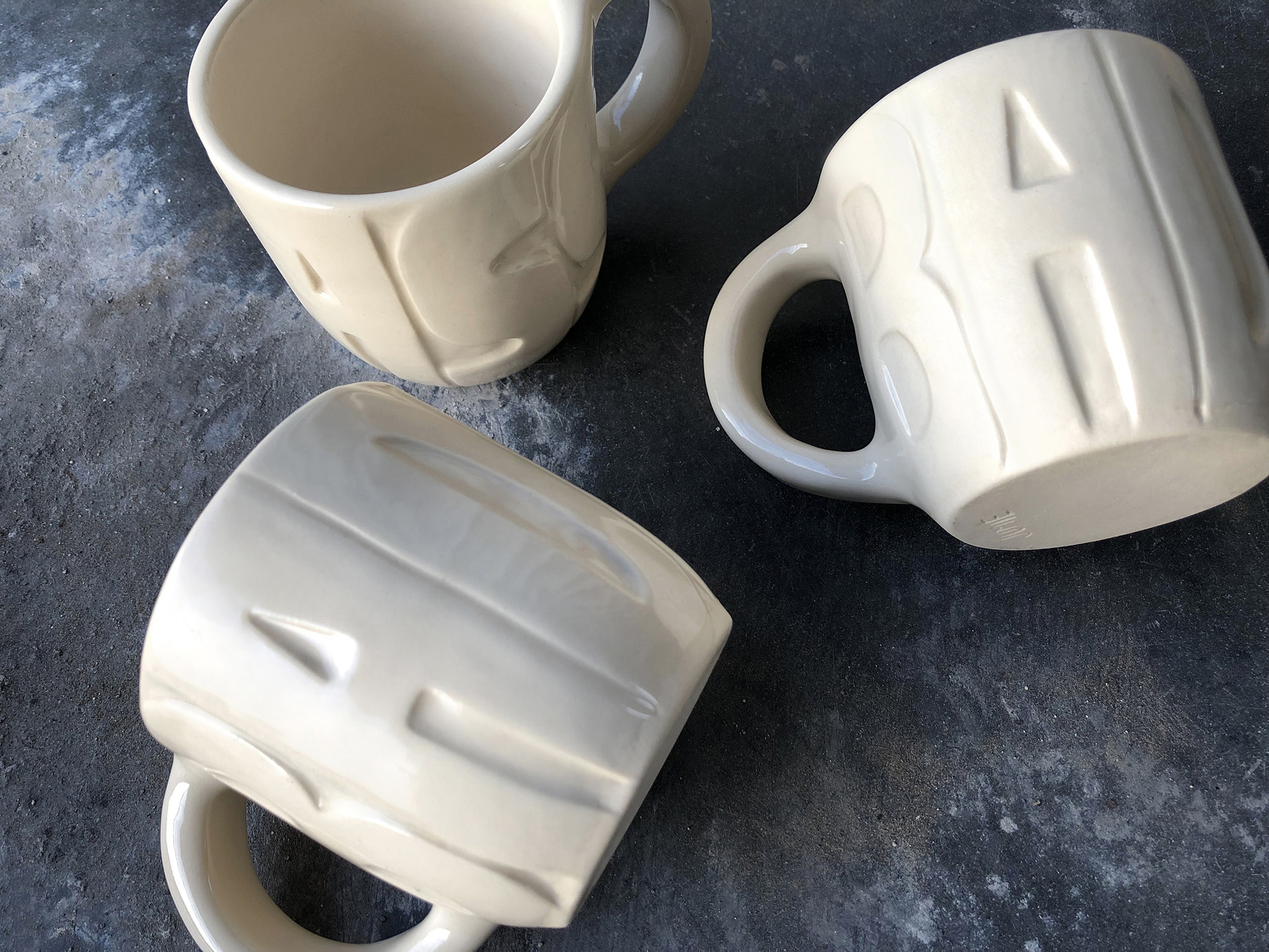 three cream colored coffee mugs with the word 'badass' carved into the outside of the mugs.