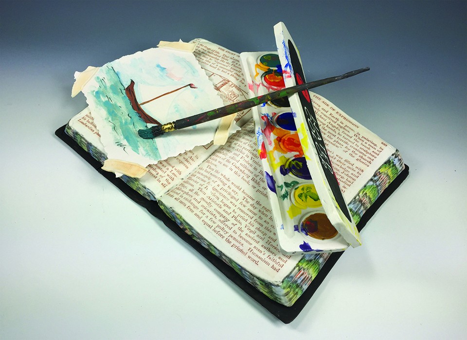 Open book with a colorful fore-edge. A watercolor set with a painbrush and a painting of a sailbot rest on top of the open book. This is all made of clay.