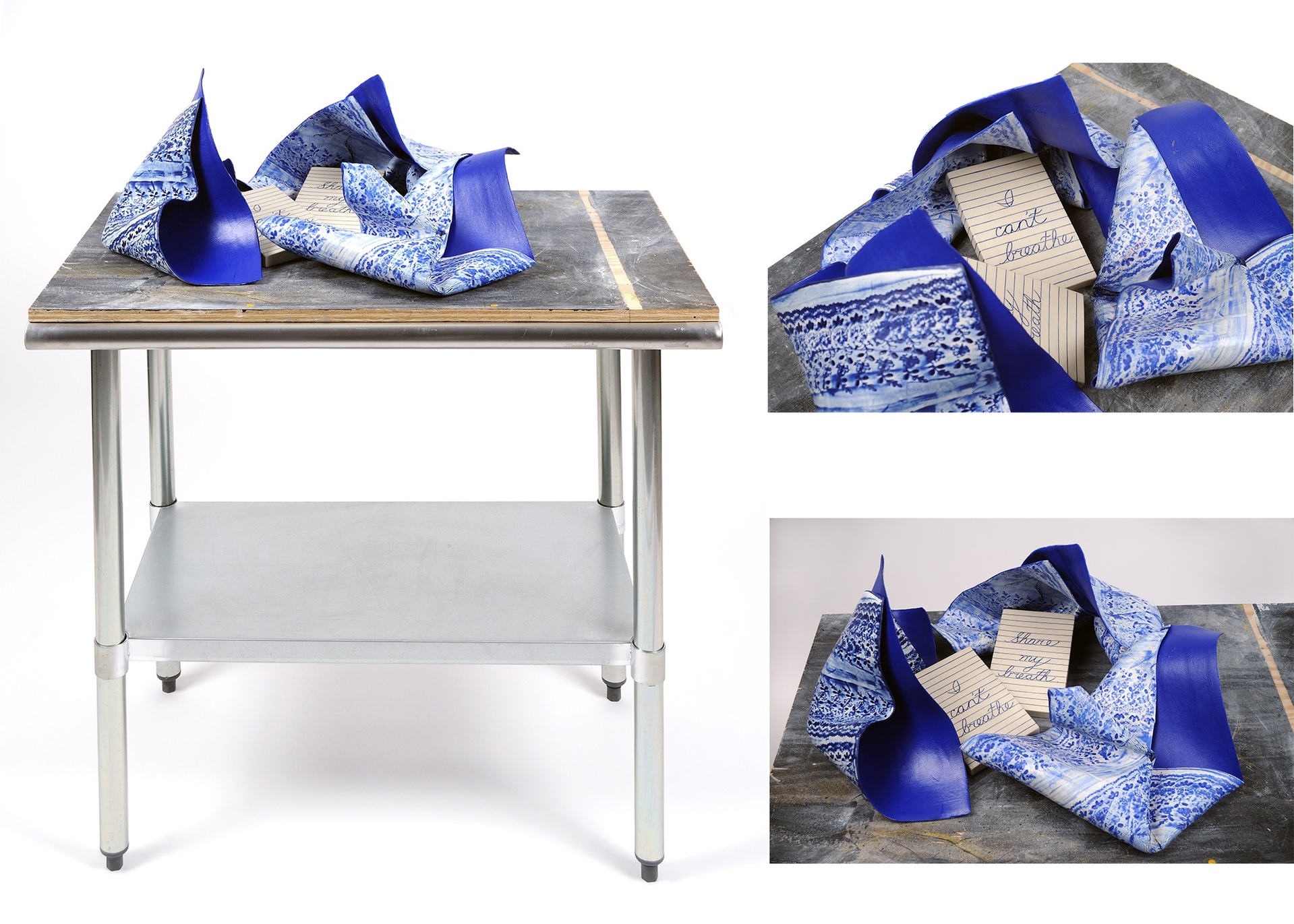 table that looks like it would be in a professional kitchen. On the table rests three pieces of blue cray that are shaped and painted to resemble bandanas. There are two note cards with cursive writing on them in the bandanas. One reads 'I can't breate' and the other says 'Share my breath'