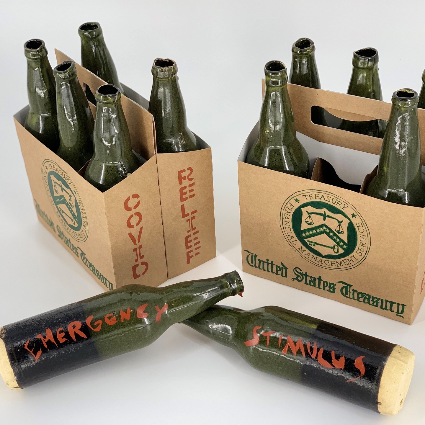 two six pack of empty glass beer bottles in cardboard boxes with the bottles stating, "Emergency" on one bottle and "Stimulus" on the other with the stamp of the United States Treasury and "COVID RELIEF" on the side.