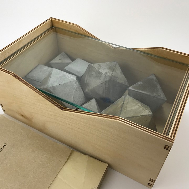 a handmade book with the title "The Radiant Republic" and enclosed in a wooden box with glass that holds weathered platonic solid cast in cement.